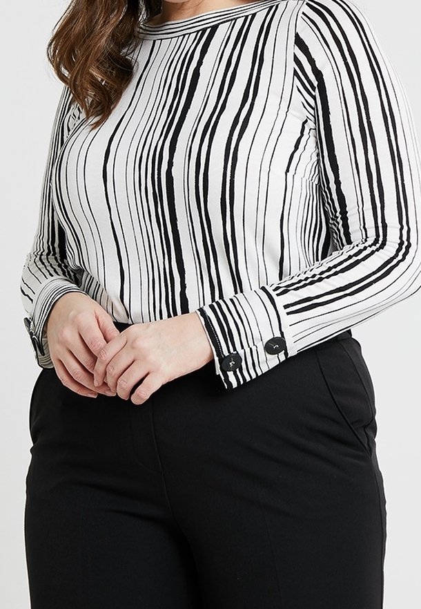 Wit shirt met lange mouwen en verticale zwarte strepen. Voorzien van manchetknoopjes en een ronde halslijn. Gecombineerd met zwarte broek.