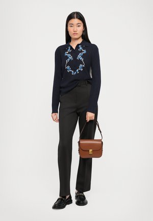 Marineblauer Pullover mit floraler Stickerei, schwarze formelle Hose, schwarze Slippers und eine braune Ledertasche mit einem goldenen Verschluss.