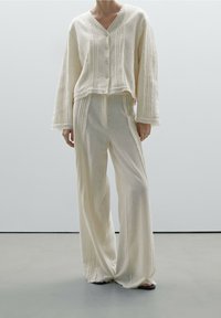 Kremowy zestaw odzieży domowej z krótką, zapinaną na guziki bluzką w teksturowane paski oraz szerokimi spodniami z pasującymi detalami.