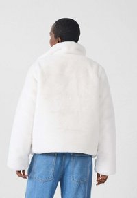 Witte nep bontjas met een hoge kraag, ontspannen pasvorm en lange mouwen, gecombineerd met blauwe denim jeans. Zachte textuur en minimalistisch ontwerp.
