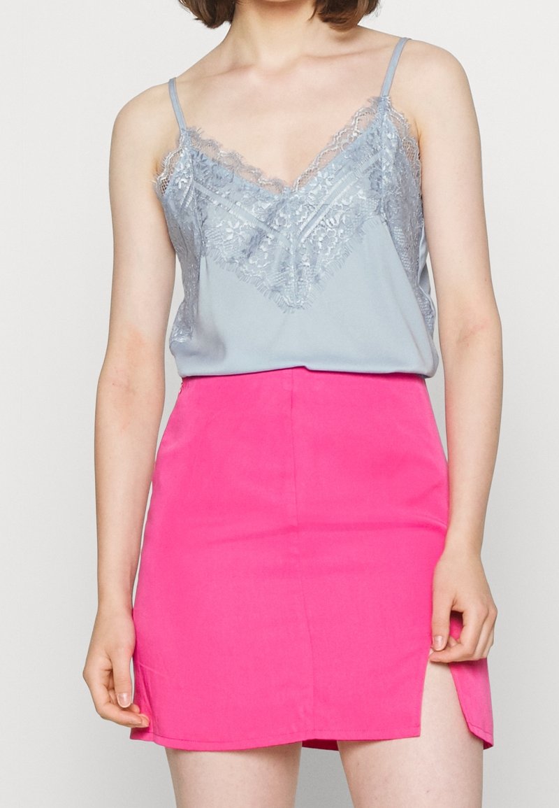 Ljusblå spetskantad linne med justerbara band, i kombination med en ljusrosa minikjol med en sidoöppning. Släta texturer.