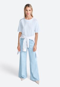 T-shirt rayé bleu clair associé à un jean large en denim clair taille haute. Chemisier blanc noué à la taille, escarpins à bout pointu.