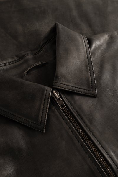 Black leather jacket feature close-up, with a collared neckline and visible zipper detail. The leather has a smooth texture and subtle sheen.