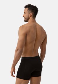 Zwarte boxershorts met een zachte elastische tailleband, met een fitted ontwerp en een gladde textuur, gedragen door een model vanuit een zijaanzicht.