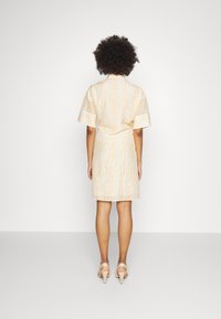 Krátké šaty s krátkým rukávem v světle oranžové barvě s vzorovaným designem. Mají pás v pase a sahají nad kolena, doplněné o tělové lodičky.