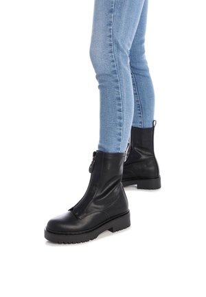 Botines de cuero negro con cierre de cremallera, suela de goma plana y detalles de costura mínimos. Combinados con unos jeans ajustados de color azul claro.