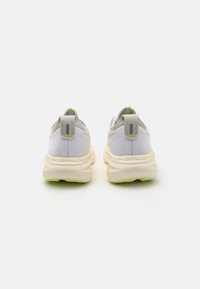 White ASICS athletic shoes with a textured mesh upper, contrasting grey accents, and a thick cream-colored sole featuring a green grip.
