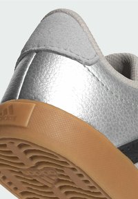 Strieborné kožené tenisky s textúrovaným povrchom, vybavené gumovou podrážkou a minimalistikým dizajnom. Výrazné prešívanie na hornej časti.