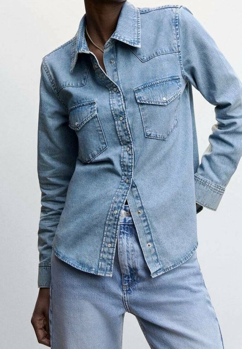 Camicia di jeans azzurro chiaro con maniche lunghe, colletto a punta, due tasche sul petto e bottoni automatici, caratterizzata da una texture liscia e una vestibilità classica.