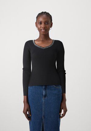 Top negro de manga larga acanalado con escote en V y un cuello decorado. Combinado con una falda de mezclilla azul con una abertura frontal.