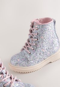 Glitrende sølvankelstøvler med lyserøde snørebånd og foring, tekstureret overdel, rund tå og kraftig gummisål med mønstret slidbane.