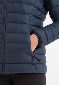 Navy puffer jacket featuring horizontal quilted sections, zippered pockets, elastic cuffs, and a smooth, shiny finish.