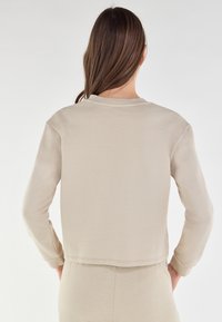 Felpa beige a maniche lunghe con collo rotondo a coste, tessuto testurizzato e orlo dritto. Presenta polsini aderenti e una silhouette rilassata.