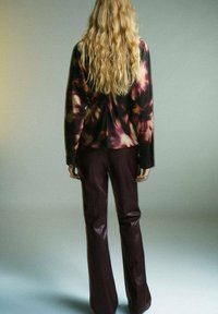 Camisa de manga larga con un patrón de tie-dye oscuro en tonos burdeos y beige, combinada con pantalones de imitación cuero burdeos de tiro alto.