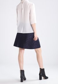 Krémová halenka s 3/4 rukávy, s volánkovým detailem u krku, v kombinaci s tmavě modrou sukní s květinovým vzorem. Černé kotníkové boty se zlatými detaily.