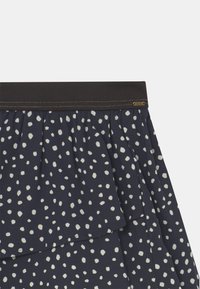 Jupe bleu marine en tissu superposé avec des pois blancs irréguliers, dotée d'une large ceinture élastique noire avec des coutures dorées.