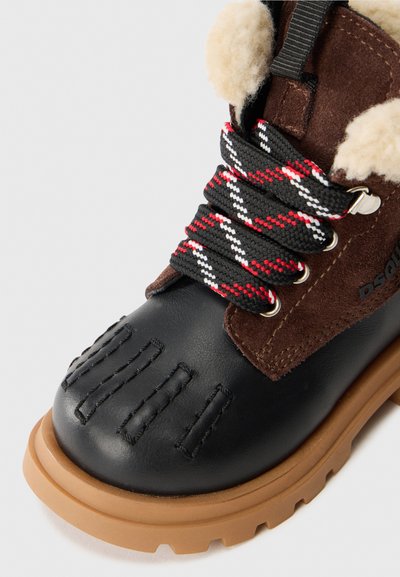 Sorte lær ankle boot med brune suede-detaljer, teksturert tå, røde og hvite mønstrede lisser, og en tan gummisåle.