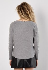 Grauer Strickpullover mit lockerer Passform, der mit verzierten Perlenakzenten an den Schultern und einem gerundeten Saum versehen ist. Strukturierter Stoff.