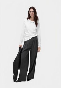 Chemise blanche à manches longues avec un col rond, associée à un pantalon charbon à taille haute et jambes larges, et une veste en cuir noire.