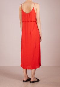 Robe rouge sans manches à la coupe fluide, dos superposé et ourlet au niveau du genou. Texture douce complétée par des sandales slides noires.