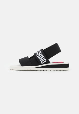 Sort-hvid sandal med elastiske stropper, med fed hvid tekst på den midterste strop og en tyk sål med slidmønster.