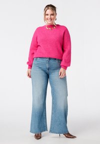 Roze gebreide trui met een ronde halslijn, gecombineerd met een wijduitlopende blauwe spijkerbroek. Accessoires omvatten een ketting in goudkleur en hoge hakken met luipaardprint.