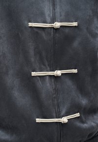 Κοντινό πλάνο σε σκοτεινό ύφασμα με τρεις οριζόντιες μπεζ κορδόνιες κλειδαριές με δεμένες θηλιές κατά μήκος μιας ραφής.