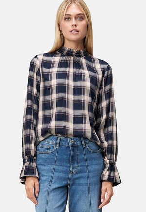 Marineblau und cremefarbene Karo-Bluse mit langen Ärmeln, gerüschtem Ausschnitt, fließendem Stoff und Glockenärmel, kombiniert mit hellblauen Jeans.