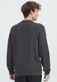 Szürke kötött pulóver kerek nyakkivágással és bordázott mandzsettákkal. Egyszerű dizájn, puha anyagból, laza szabással és minimális díszítéssel.