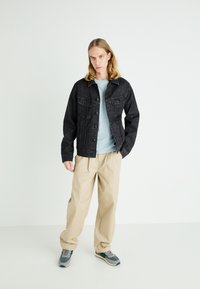Chaqueta de mezclilla negra con bolsillos frontales, camiseta de color azul claro, pantalones beige y zapatillas grises. Conjunto sencillo y casual con texturas visibles.