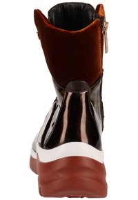 Bottines noires et brunes en matériau brillant et en velours texturé, avec une semelle blanche et rouge et une fermeture éclair sur le côté pour un accès facile.