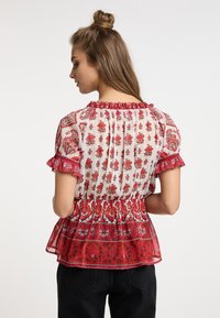 Blomsterbluse i gennemsigtig hvid stof med røde mønstre, flæseærmer og peplum talje. Har indviklede blomster detaljer.