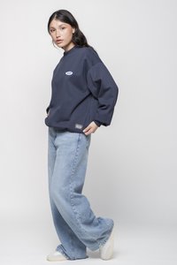 Felpa blu marina con polsini a coste, caratterizzata da un piccolo logo sul petto. Abbinata a jeans a gamba larga blu chiaro e sneaker bianche.