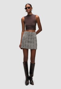 Brun cropped top, houndstooth mini nederdel, knæhøje mønstrede støvler. Tætsiddende design, glat tekstur og kontrasterende farver.