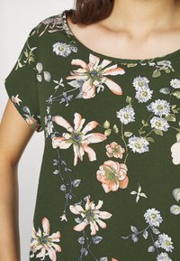 Groen top met bloemenpatroon van lichtgewicht stof, met een ronde halslijn en korte mouwen, versierd met verschillende bloemen in roze, wit en blauw.