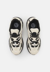 Sneaker mit einer strukturierten cremfarbenen Oberseite, schwarzen Akzenten und Schnürsenkeln. Verfügt über ein rundes Logo, einen silbernen Streifen und eine gemusterte Außensohle.