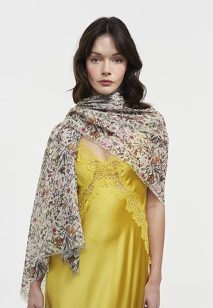 Ženska s temnimi lasmi nosi rumeno obleko z čipkastim robom in lahkoten šal z rožnatim vzorcem, ki ji je prevržen čez ramena, na enobarvni podlagi.