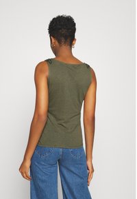 Top sin mangas verde oliva con acentos texturizados en los hombros, diseño ajustado y tela suave. Combinado con vaqueros de pierna ancha azules.