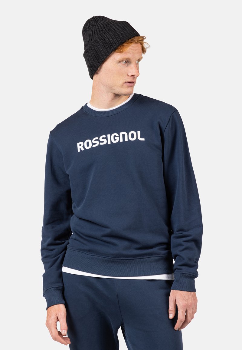 Felpa blu navy con testo bianco "ROSSIGNOL", realizzata in morbido tessuto. Presenta un classico colletto rotondo e polsini e orlo a costine.