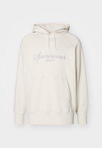 Krémová mikina s kapucí na šňůrky, přední kapsou a vyšívaným textem "Sportswear by PUMA" v světle modré barvě. Měkká látka, uvolněný střih.