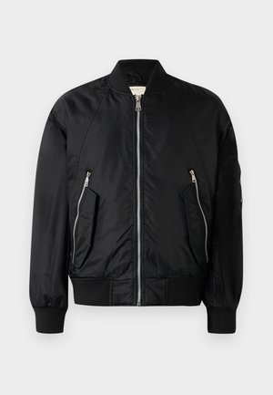 Veste bombers noire en nylon lisse. Dotée d'une fermeture éclair sur le devant, de deux poches latérales inclinées et de poignets et ourlet côtelés. Design simple.
