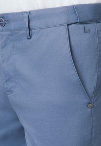 Jasnoniebieskie dopasowane spodnie wykonane z teksturowanej tkaniny. Posiadają dwie kieszenie, zapięcie na guzik oraz subtelny akcent logo na pasku.