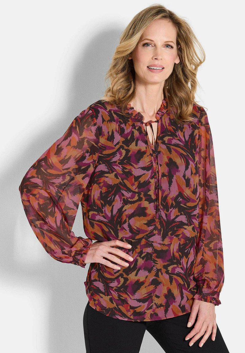 Durchsichtige Bluse in mehreren Farben mit einem blumigen Muster in Schattierungen von Lila, Orange und Schwarz, mit einem voluminösen Halsausschnitt und langen, gerafften Ärmeln.