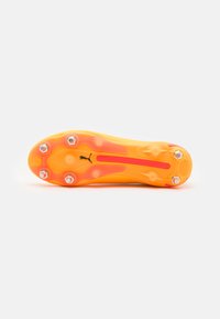 Bright yellow football boot sole with orange accents, featuring six metallic studs and a central groove, designed for traction and stability.