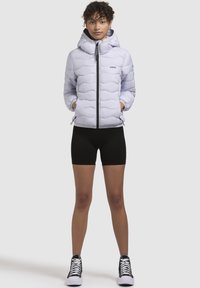 Light gray puffer jacket with a hood, featuring a wave quilt pattern and zip closure. Worn with black shorts and high-top sneakers.