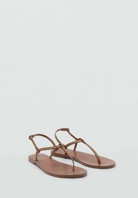 Sandali piatti marroni con un design minimalista, caratterizzati da cinturini sottili, piccole borchie e una suola piatta. Il materiale sembra sintetico e liscio.