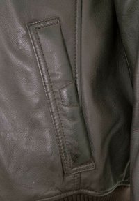 Dunkelbraune Lederjacke mit strukturiertem Finish, ausgestattet mit einer flachen Tasche auf der linken Seite und geripptem Stoff am unteren Rand.