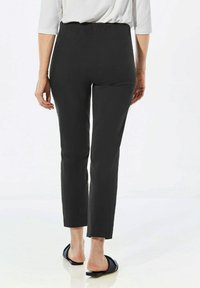 Pantalons noirs taille haute au design ajusté et longueur cheville. Tissu lisse avec un léger brillant. Associés à des sandales foncées.