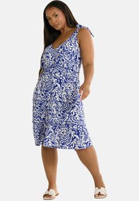 Blå och vit blommig klänning med V-ringning, justerbara band och ett lager på lager-skjort, tillverkad av lättviktig tyg.