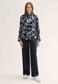 Floral long-sleeve shirt in navy with white, green, and red patterns, paired with wide-leg black trousers and white sneakers.